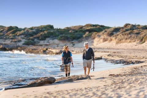 Grandfather and grandson walking on the beach with fishing poles in Western Australia