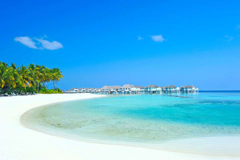Over water villas at resort with pristine white sand beach, clear turquoise water and blue skies in the Maldives