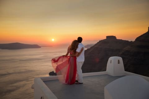 A couple watches the sunset over Santorini, Greece